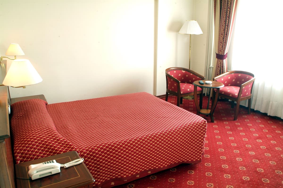 A hotel room with a bed, a bedside table with a phone, two chairs, a small table, and a lamp.