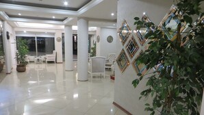 Un vestíbulo amplio con piso de baldosas brillantes, mobiliario blanco y espejos decorativos en las paredes.
