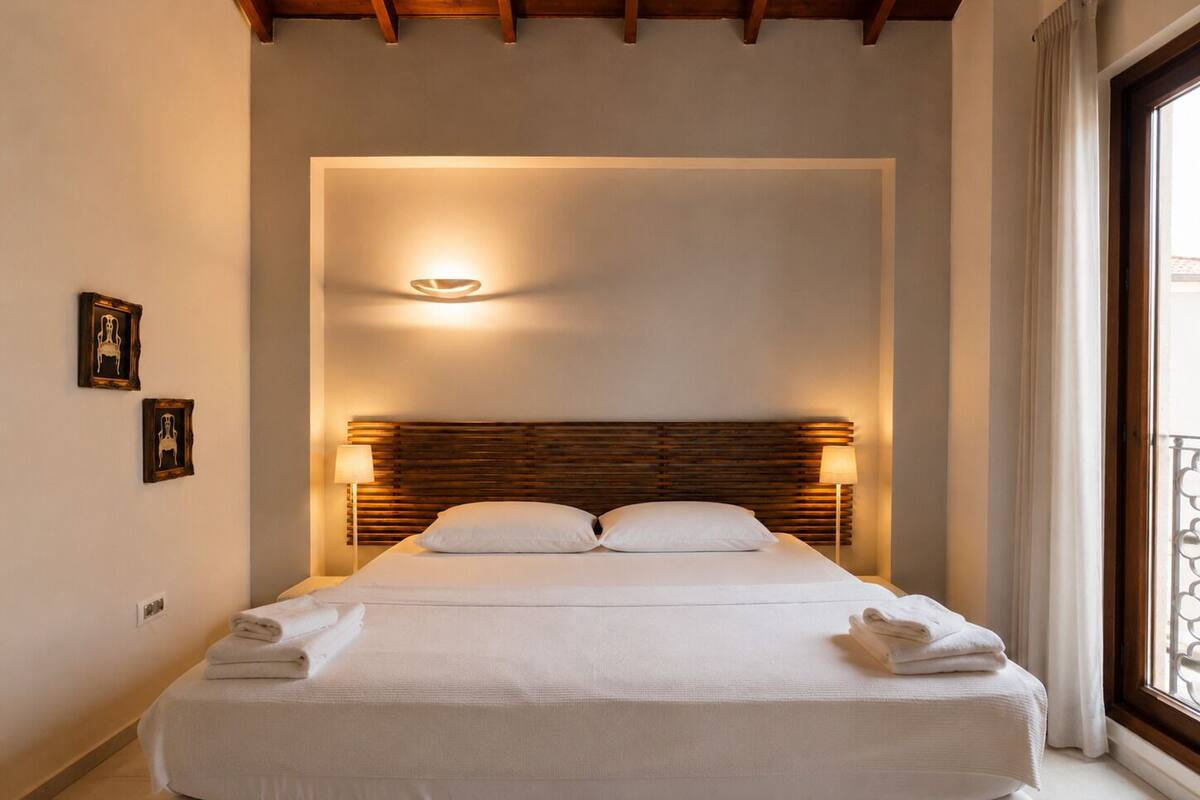 A hotel room with a bed, bedside lamps, and a view through a window.