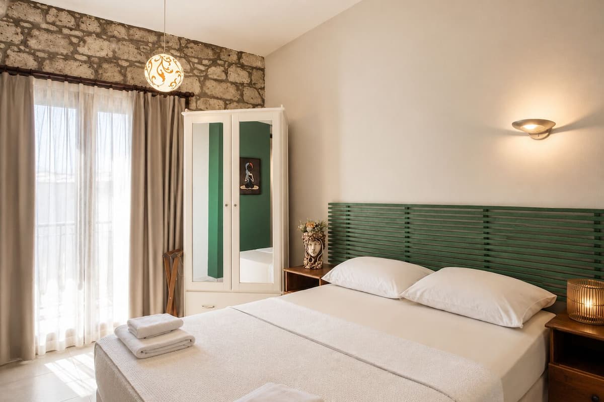 A bedroom with a bed, nightstands, a wardrobe, and a stone wall.