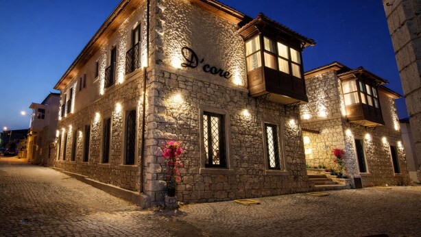 Um edifício de pedra com a placa 'D'core', iluminado à noite, com janelas brilhantes e rua de paralelepípedos.