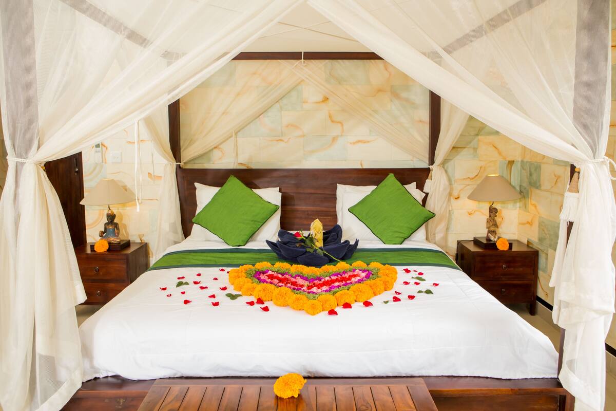 A bed with a canopy, green pillows, a decorative flower arrangement, and a wooden headboard.