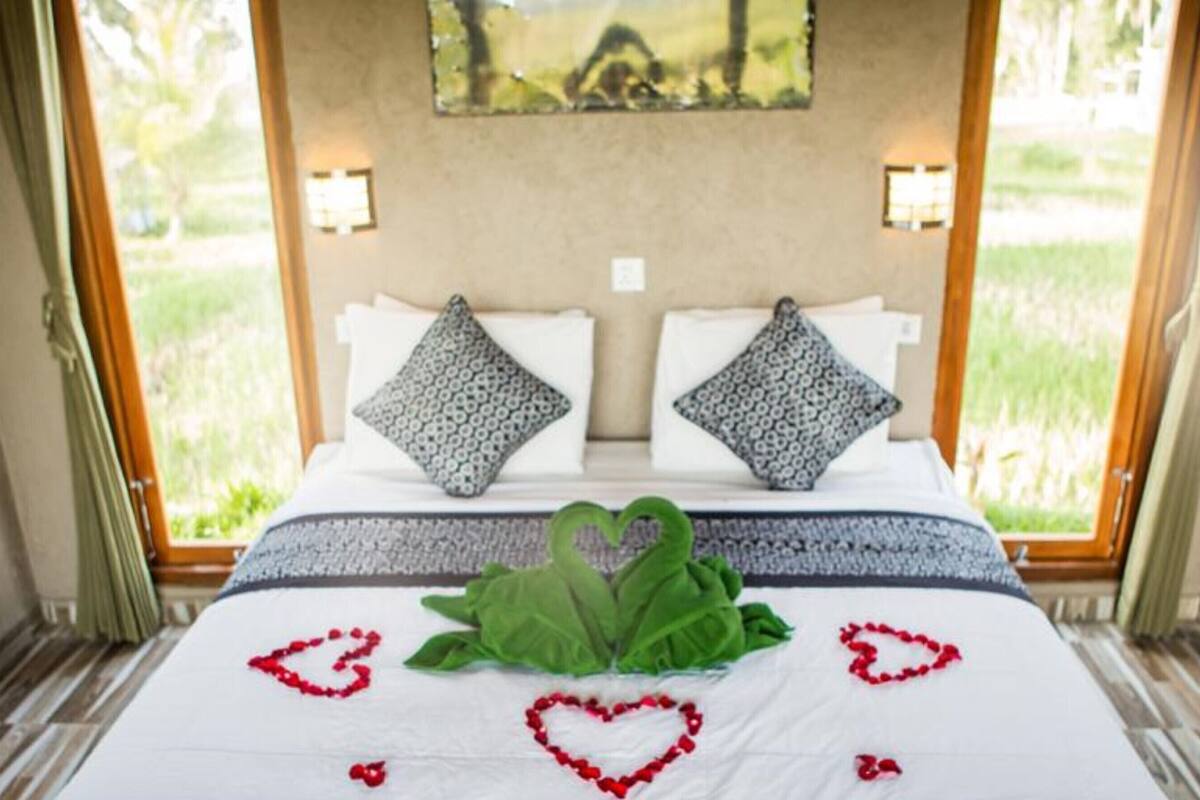 A bed with a white bedspread, two patterned pillows, and a decorative swan made of leaves and red beads.