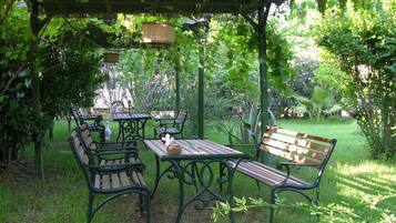 Un patio jardín con una mesa y bancos de madera, rodeado de abundante vegetación y una estructura de pérgola.
