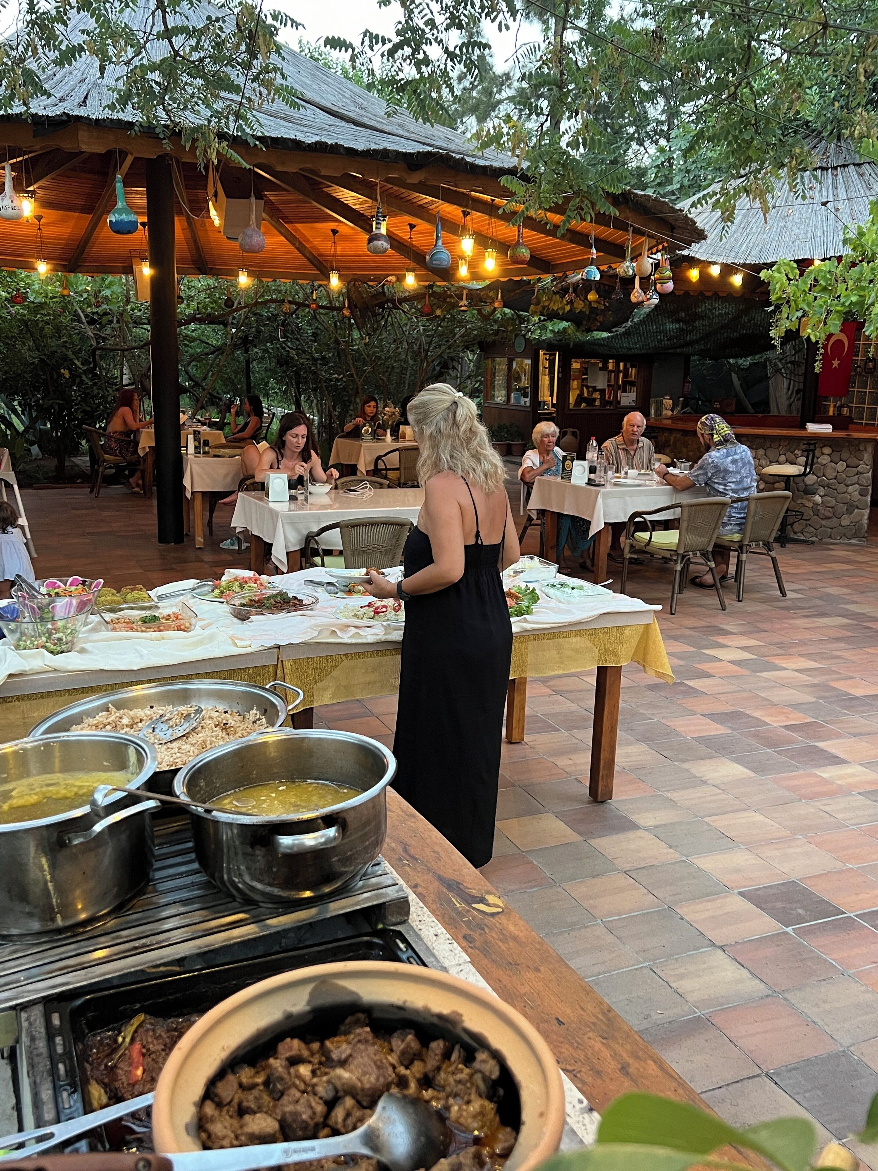 An outdoor dining area with multiple tables, a buffet with various dishes, and a grill station.