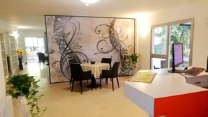 A modern reception area with a white desk, black chairs, and a decorative wall. - Hotel Rita (Cervia)