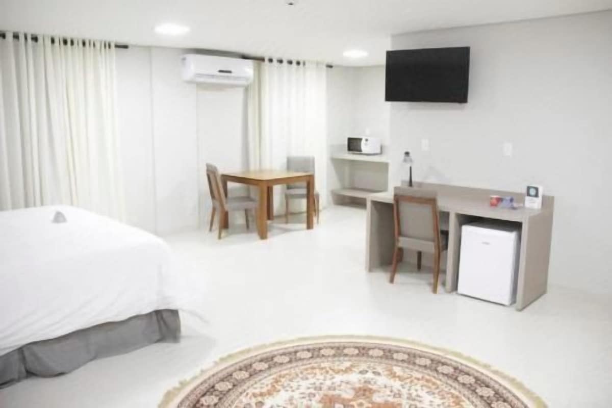 Une chambre d’hôtel équipée d’un lit, d’un bureau, d’une chaise, d’un petit réfrigérateur et d’un téléviseur fixé au mur.
