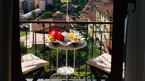 Un balcón con una mesa dispuesta para el desayuno, con vistas a un paisaje urbano que incluye edificios y una masa de agua.