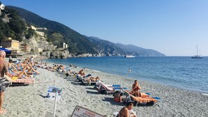 Una playa con gente tomando el sol y nadando, un barco en el agua y edificios a lo largo de la colina.