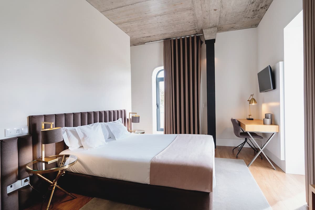 Ein modernes Hotelzimmer mit einem großen Bett, einem Schreibtisch, einem Sessel und einem Fernseher.