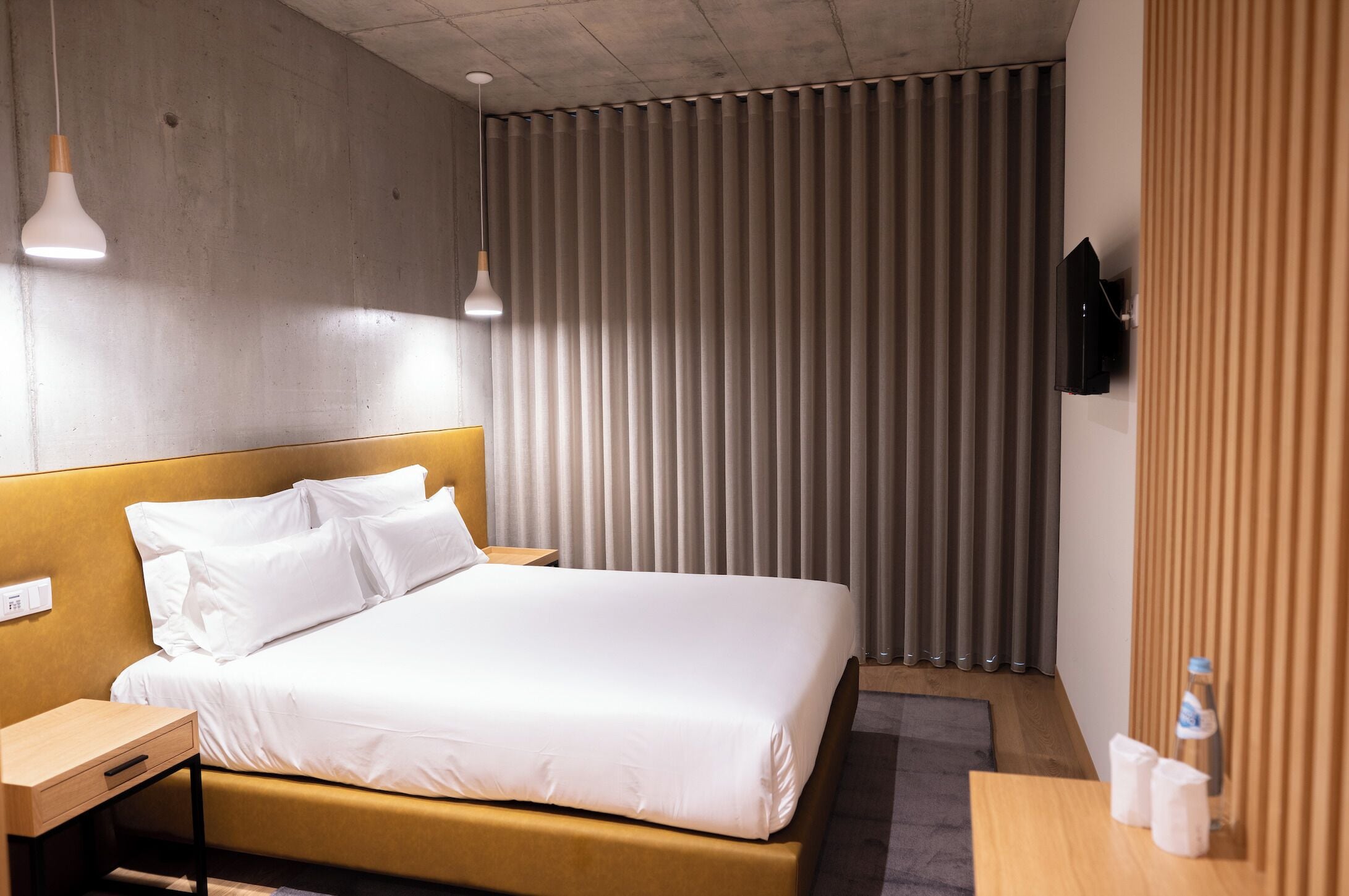 Una habitación de hotel con cama, mesitas de noche, televisor y ventana con persianas.