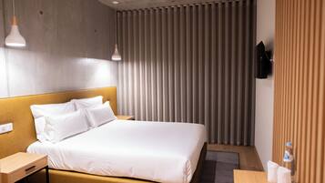Una habitación de hotel con cama, mesitas de noche, televisor y ventana con persianas.