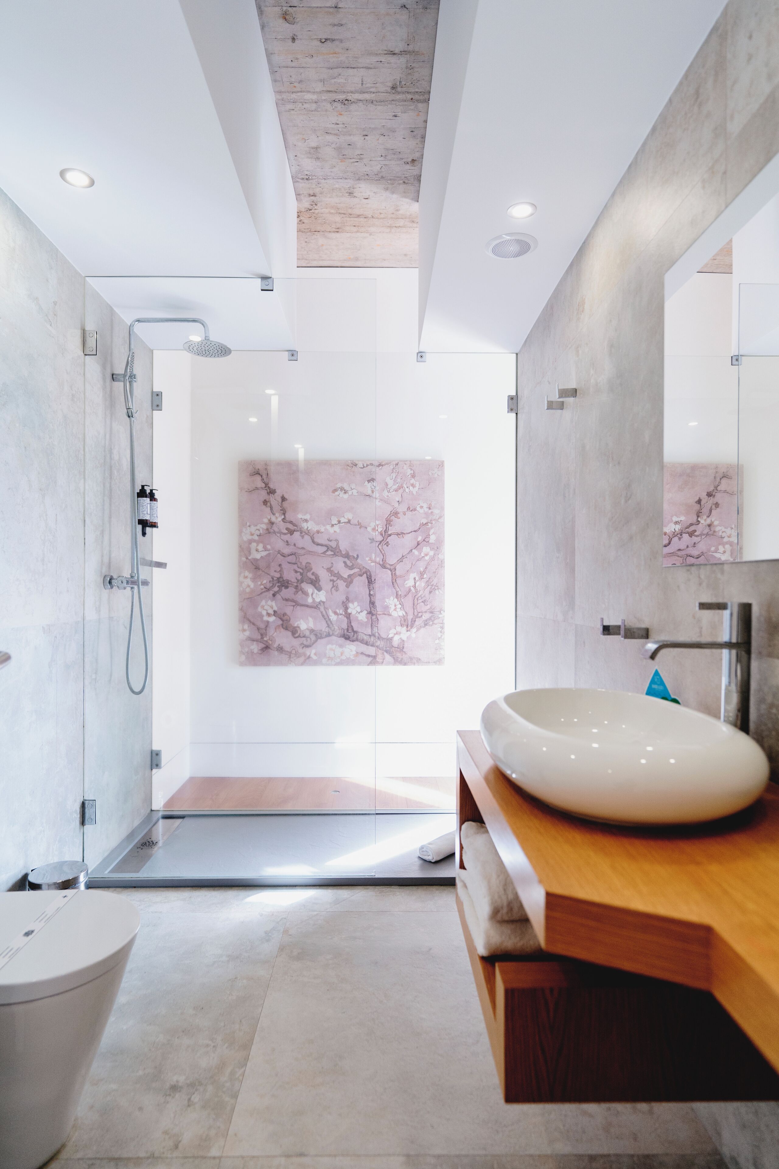 A modern bathroom with a large mirror, a wooden vanity, a marble wall, and a shower area.