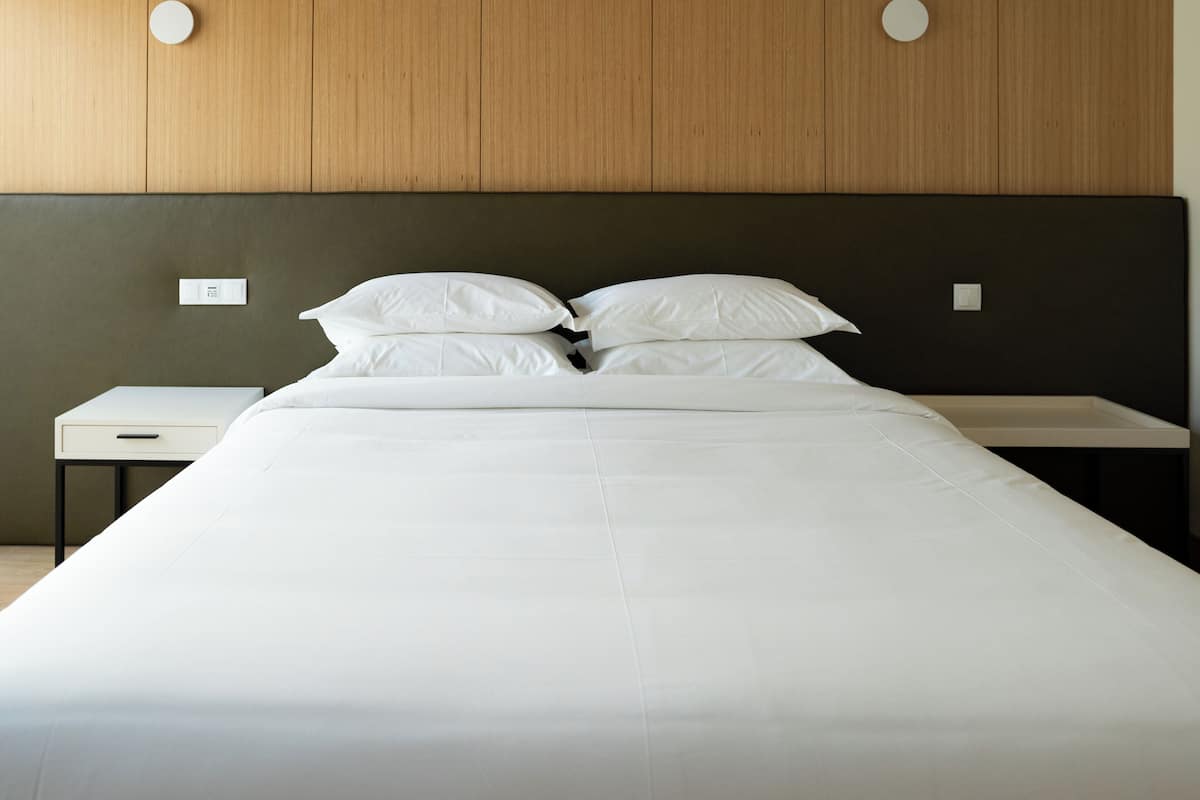 Ein Bett mit weißen Leinen, ein hölzernes Kopfende und ein Nachttisch mit Schublade.