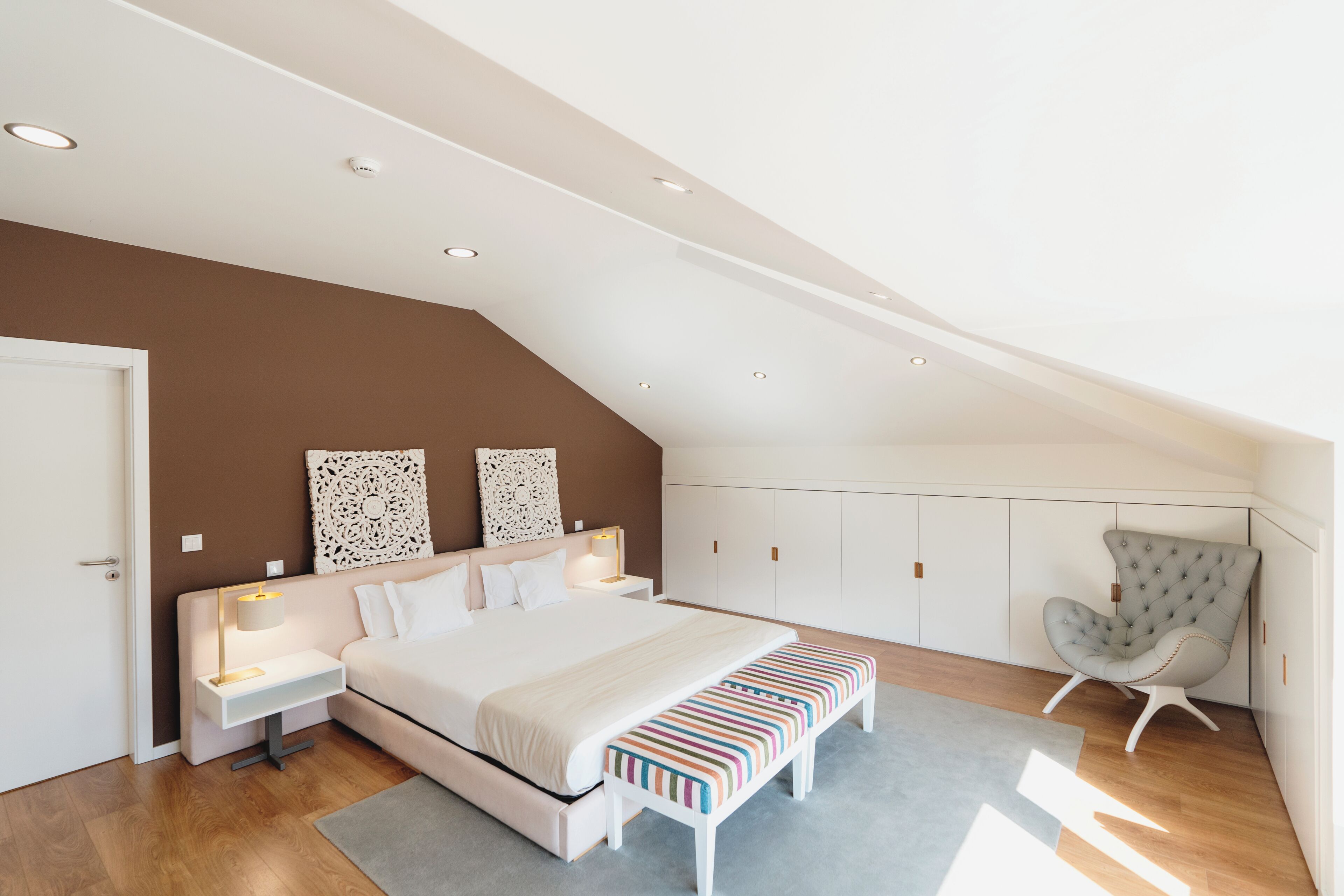 A bedroom with a bed, bedside tables, a bench, a chair, and a wardrobe.