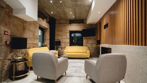 Een modern interieur met stenen muren, een gele bank, twee fauteuils, een ronde salontafel en een wandpaneel van hout.