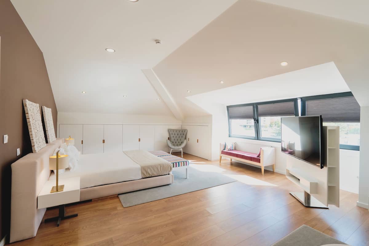 Ein modernes Schlafzimmer mit Bett, Nachttisch, Stuhl, Fernseher und großen Fenstern.