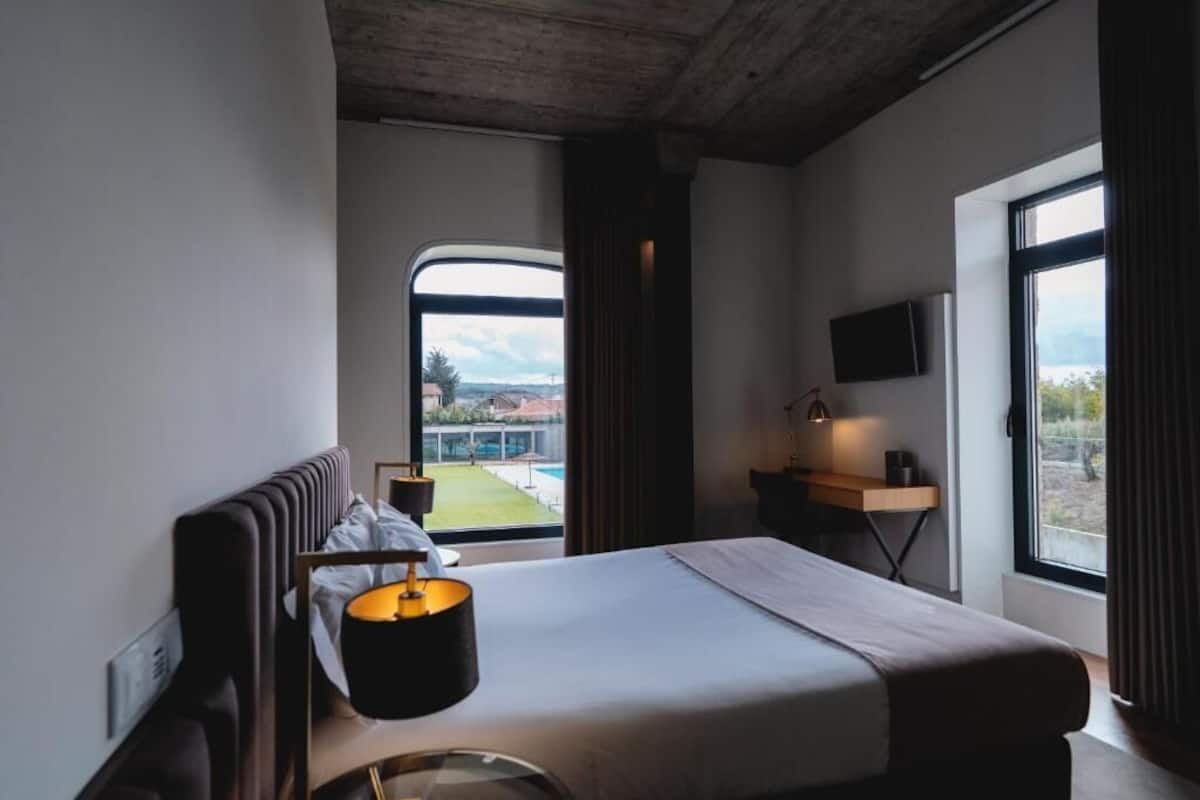 Ein modernes Hotelzimmer mit einem großen Bett, einem Schreibtisch, einem Fernseher und Blick auf einen Pool und Gebäude.