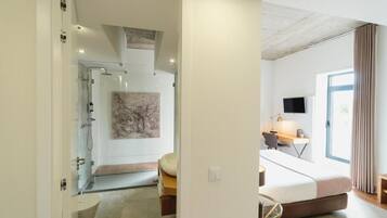 A modern hotel room with a bed, desk, and a shower area.