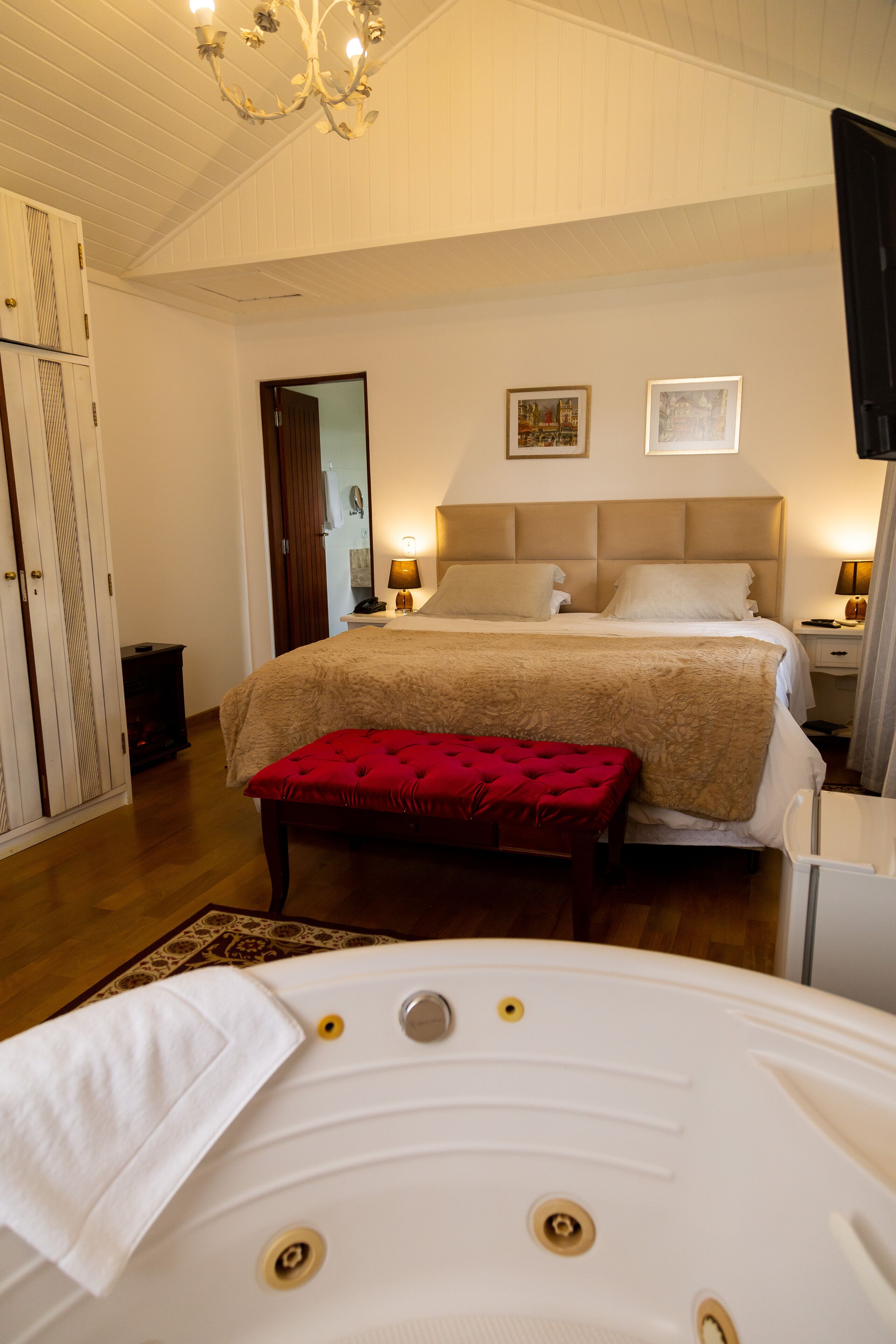 Une chambre à coucher avec un grand lit, un banc rouge, une baignoire blanche et un lustre.