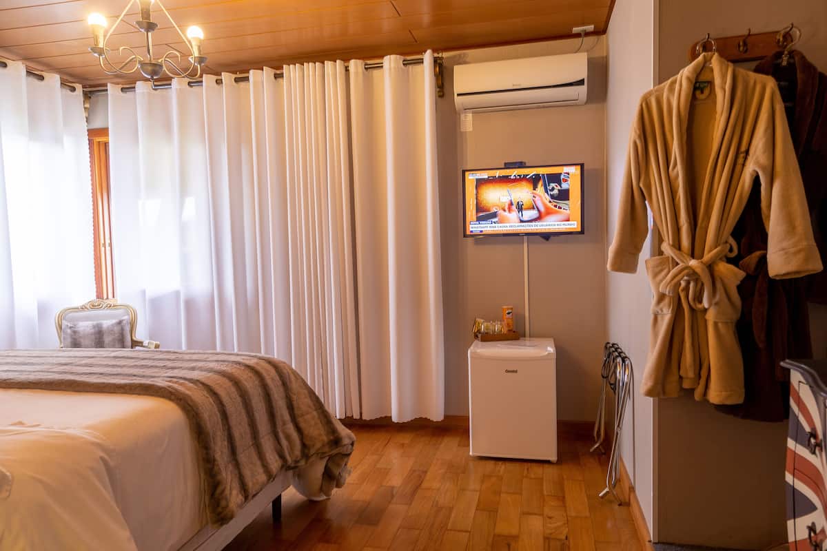 A hotel room with a bed, a TV mounted on the wall, a robe hanging on a rack, and an air conditioning unit.