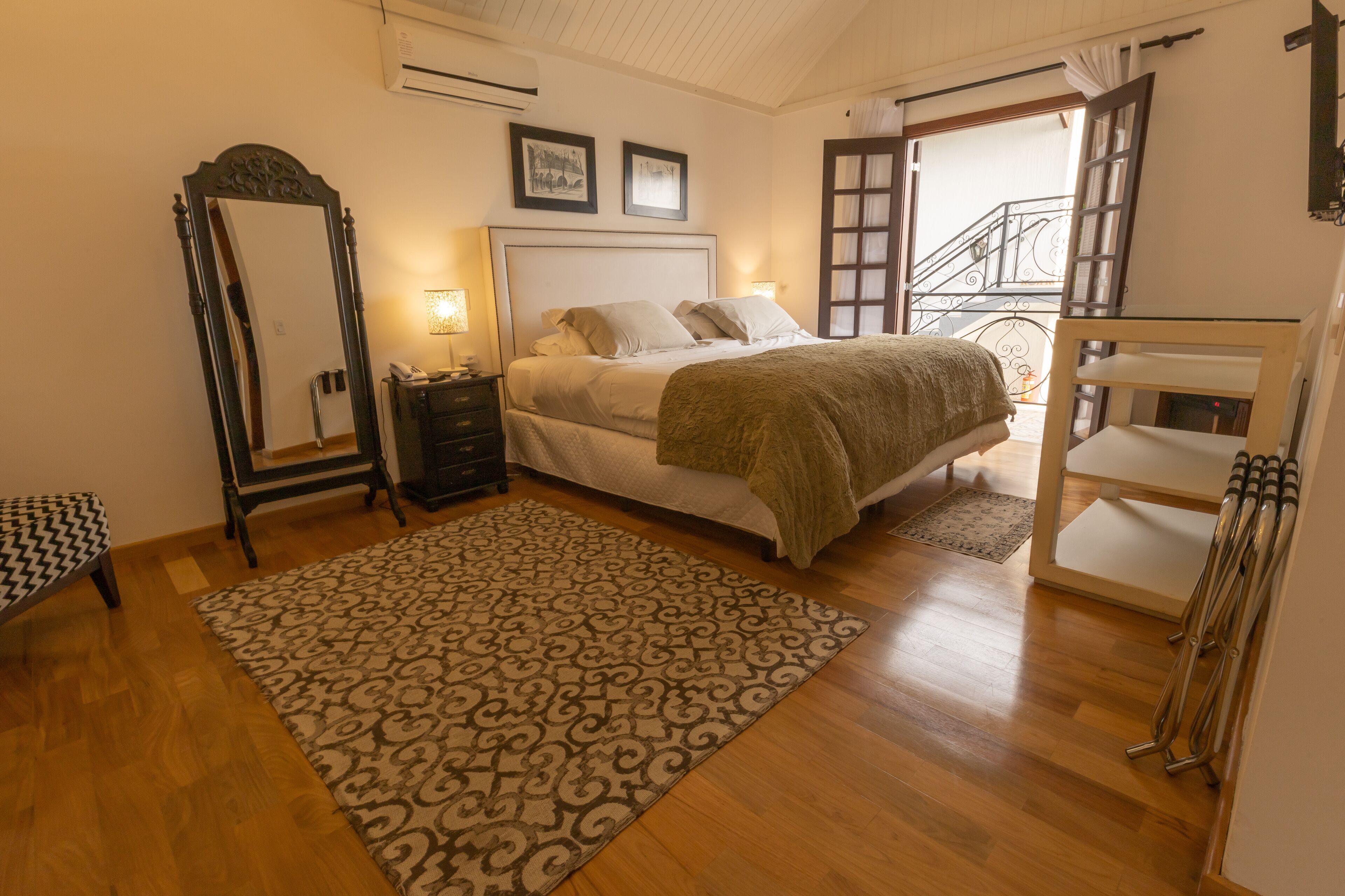 A bedroom with a bed, bedside tables, a mirror, a patterned rug, and a wooden floor.