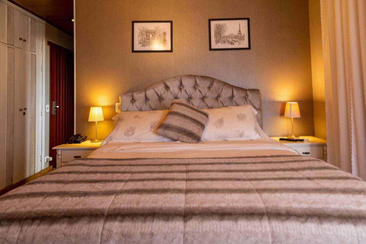 A hotel room with a large bed, two bedside lamps, a telephone, and framed pictures on the wall.