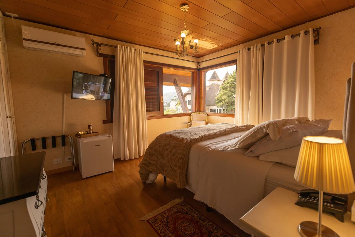 A bedroom with a bed, bedside lamp, and a TV mounted on the wall.