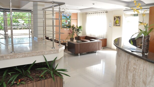 A hotel lobby with a reception desk, seating area, staircase, and potted plants.