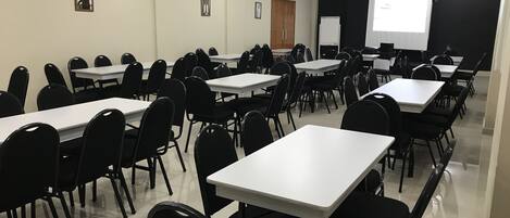 A conference room with multiple tables and chairs, a whiteboard, and a projector screen.