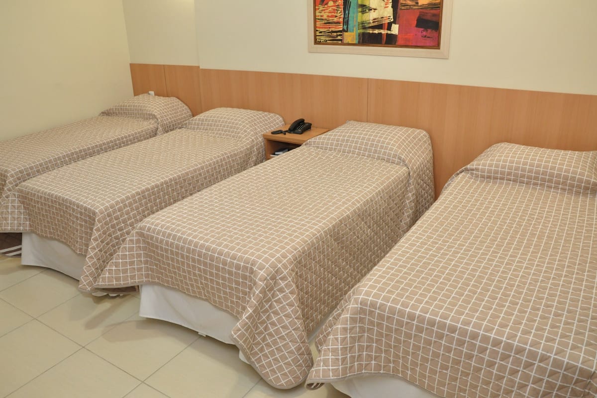 Habitación de hotel con tres camas individuales, cada una con cabecera de madera y mesita de noche con teléfono.