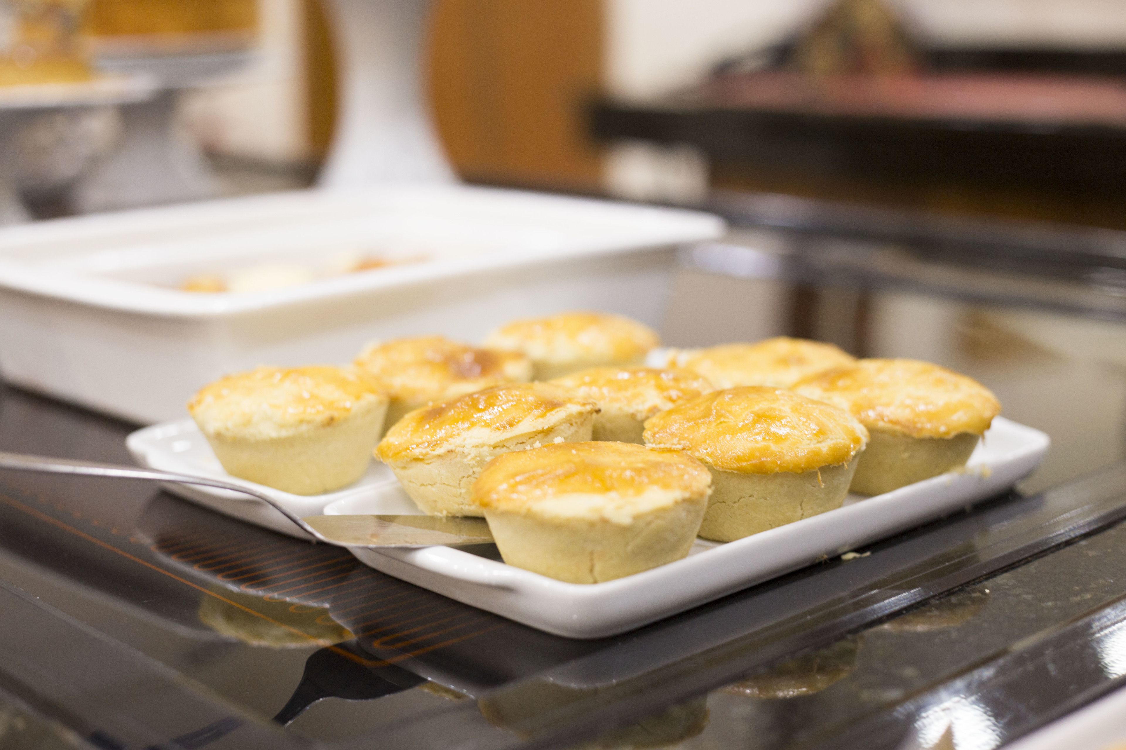 Uma travessa retangular branca com produtos de panificação dourados, possivelmente muffins ou doces, sobre uma superfície preta refletora.