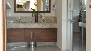 A modern bathroom with a granite countertop, a large mirror, and a glass shower enclosure.