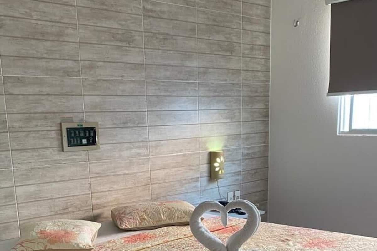 A bed with a floral bedspread, a swan-shaped pillow, and an air conditioning unit above.