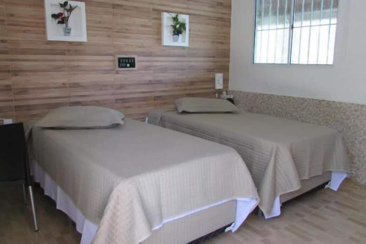 A room with two beds, a wooden wall, a window, and a clock.