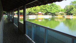 A covered walkway with glass railings overlooking a calm body of water, surrounded by lush greenery and a few structures. - Resort Hotel Atlantic City Náutico Clube (Teresina)