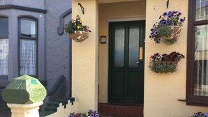 Una entrada de edificio con una puerta verde, cestas de flores en la pared y escalones que conducen a la puerta.