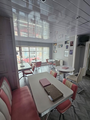 A modern office space with multiple tables and chairs, a large window with blinds, and a flat-screen TV mounted on the wall. - The Benson (Blackpool)