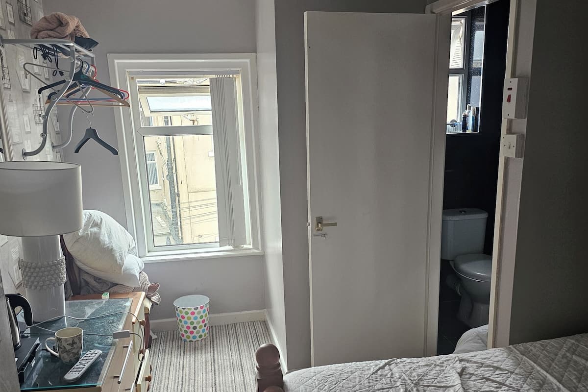 Un dormitorio con cama, escritorio con lámpara, ventana y puerta que da a un baño.