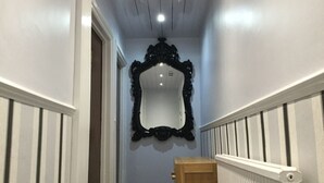 Un pasillo con un espejo negro ornamentado en la pared, una silla de madera y un radiador.