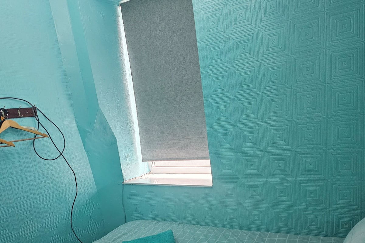 Un dormitorio con una cama individual, una ventana y una estantería en la pared.