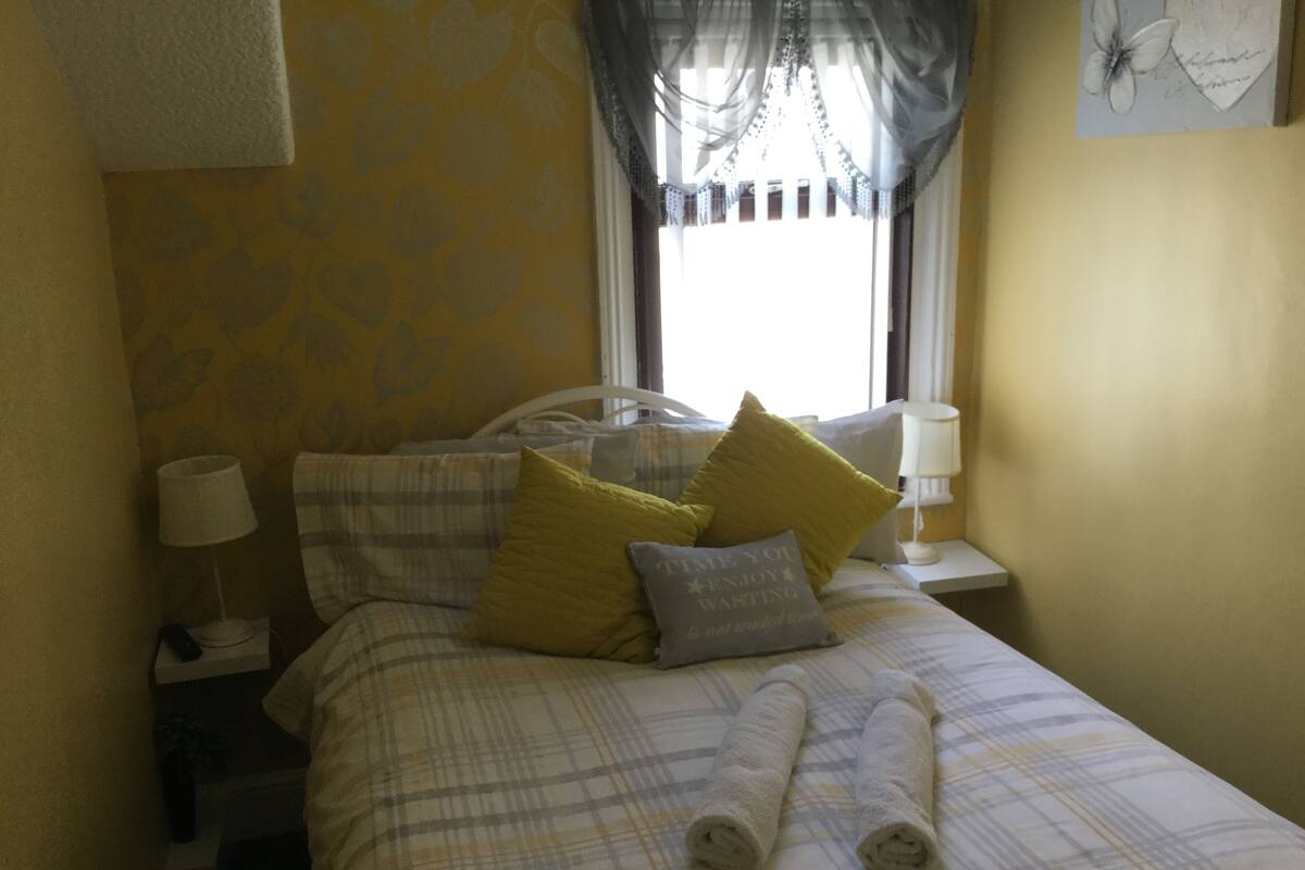 Una cama bien hecha con ropa de cama escocesa, dos almohadas y toallas enrolladas.