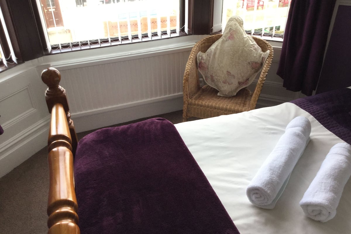Un dormitorio con una cama, un plaid morado y una almohada blanca.