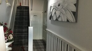 Un pasillo con una escalera, una puerta blanca y un cuadro grande con motivos florales en la pared.