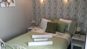 Una cama bien hecha con ropa de cama verde y blanca, dos mesitas de noche con lámparas y una pared con un papel tapiz de estampado geométrico.