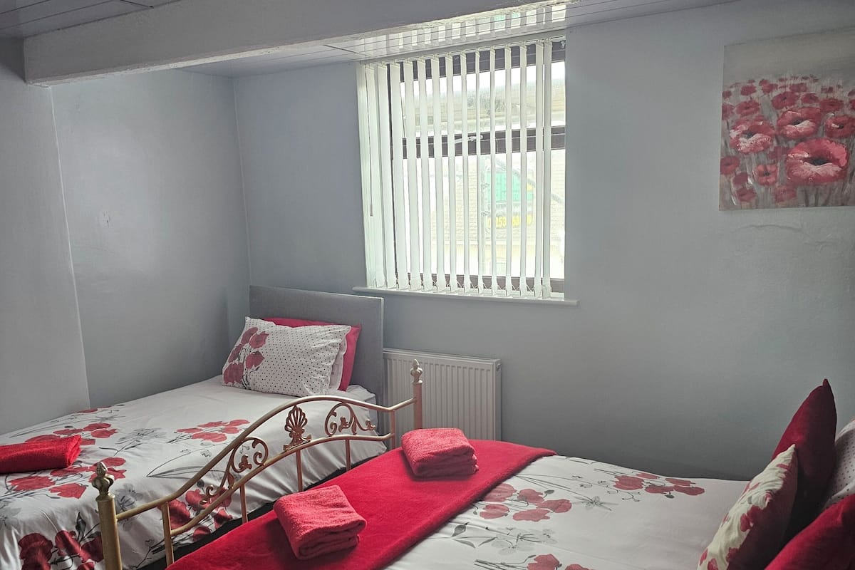 Un dormitorio con dos camas, una ventana con persianas, un radiador y un cuadro en la pared.