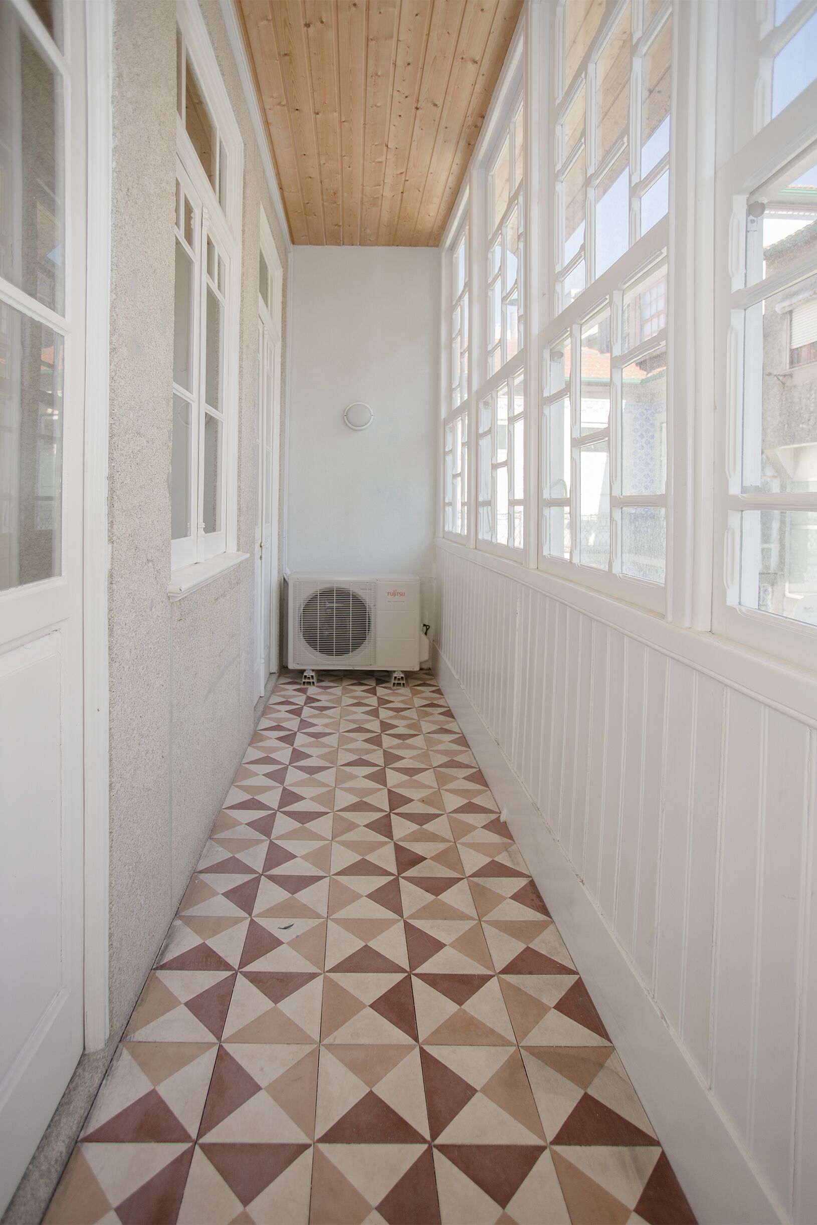 A narrow hallway with a geometric patterned floor, white walls, and large windows on one side.