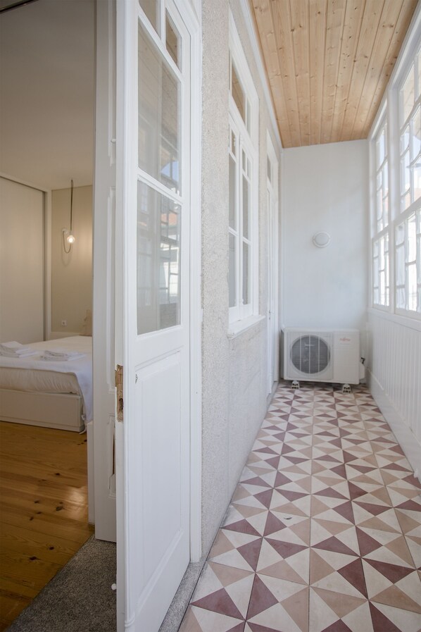 A narrow hallway with a geometric patterned floor, white walls, and a wooden ceiling. - Liiiving in Porto - Bolhão Market Apartment II (Porto)