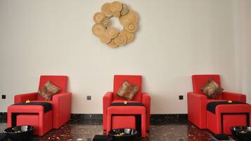 Una habitación con tres sillones de masaje rojos, cada uno con una bandeja negra y un cojín decorativo. Una obra de arte de madera adorna la pared sobre los sillones.