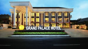 The exterior of the Grand Palace Hotel with a grand entrance, large columns, and a well-lit facade.